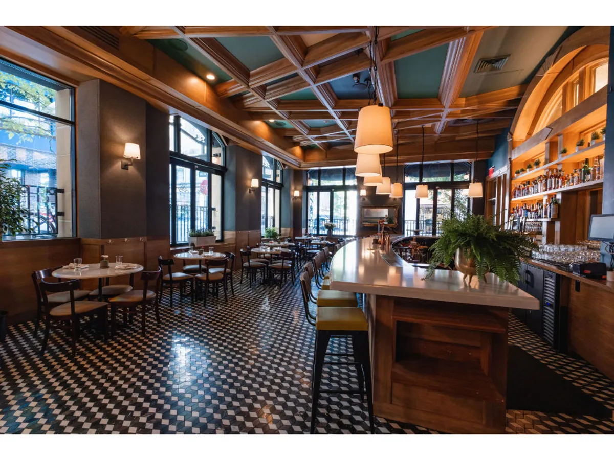 A modern bar setting with a sleek counter, contemporary hanging light fixtures, and neatly arranged dining tables. The mood is sophisticated yet casual, suggesting a welcoming place to unwind after a long day of work or meetings.