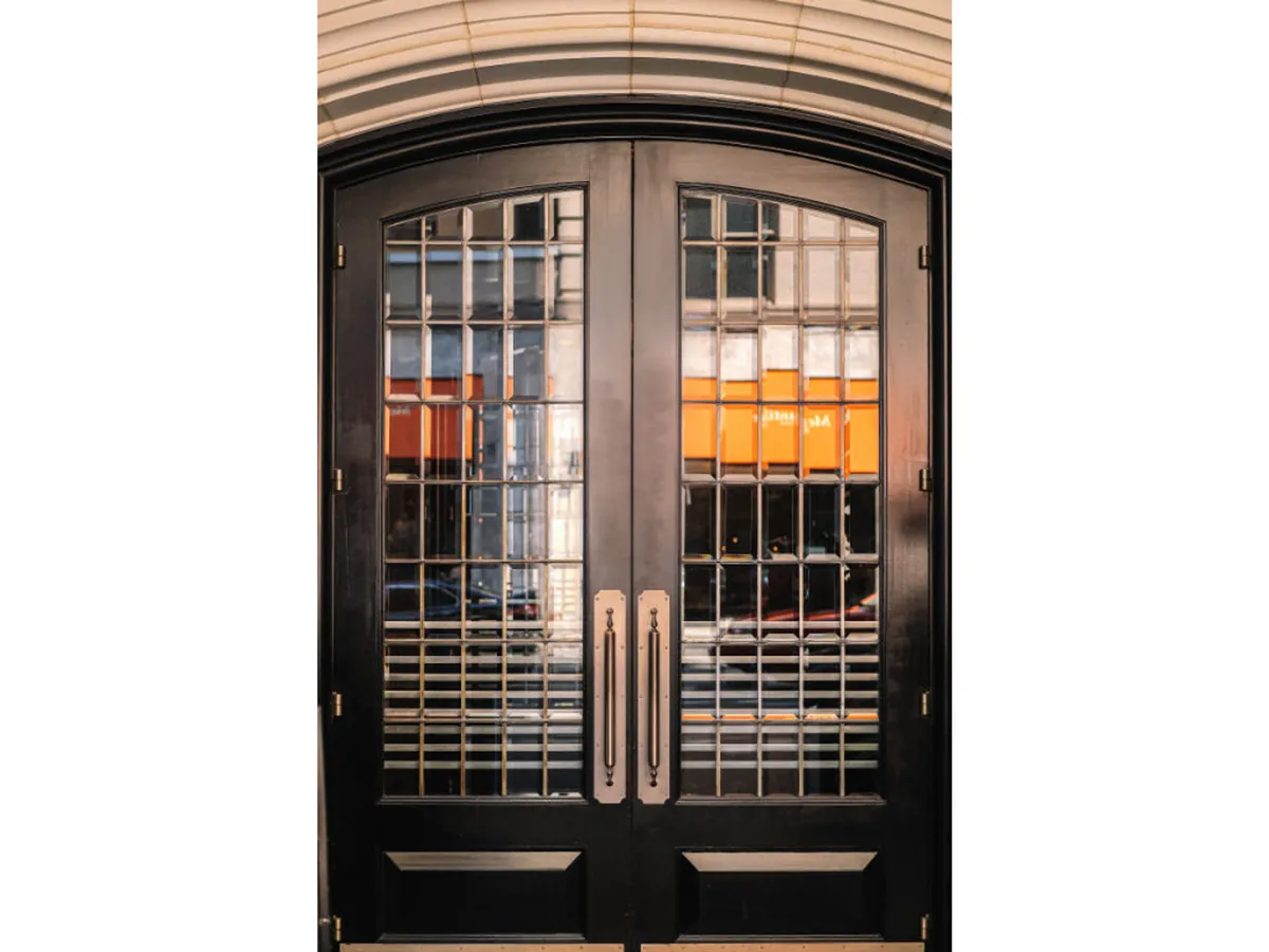 A close-up of ornate double doors with intricate glasswork and elegant handles, suggesting a luxurious entryway. The doors create a sense of anticipation, inviting guests to step into or out of the hotel and into the city.