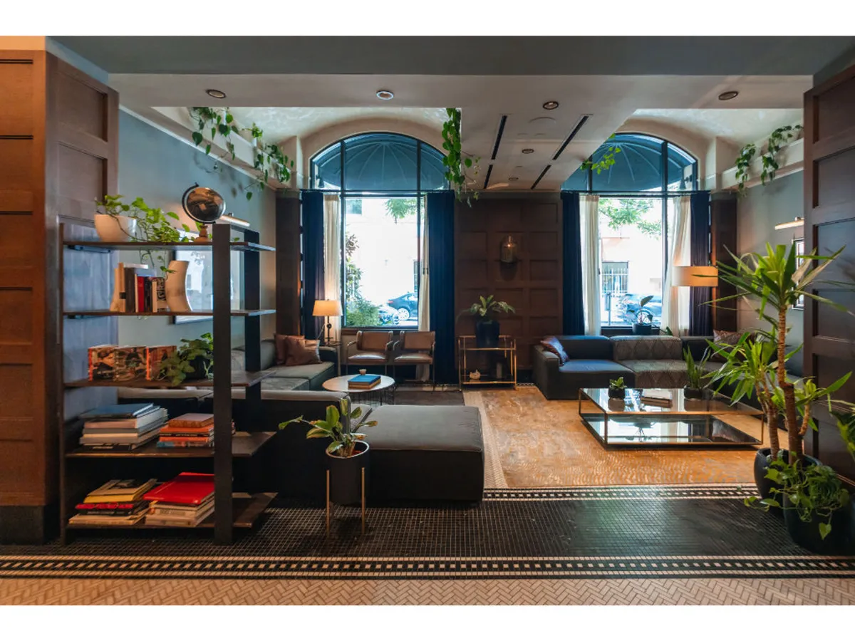 A versatile space with comfortable seating, bookshelves filled with books and plants, and expansive windows bringing in natural light. The area invites reading, working, and relaxing while surrounded by thoughtful decor.