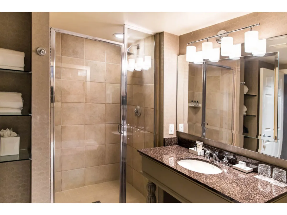 This image showcases a serene bathroom featuring a shower area, a vanity with a sink, a large mirror, and stylish light fixtures. The slate flooring and soft, ambient lighting create a tranquil setting, while the spacious shower and premium vanity emphasize luxury and comfort. The reflective surface of the mirror and the gentle glow from the lights accentuate the spa-like atmosphere, making the space inviting for self-care routines.