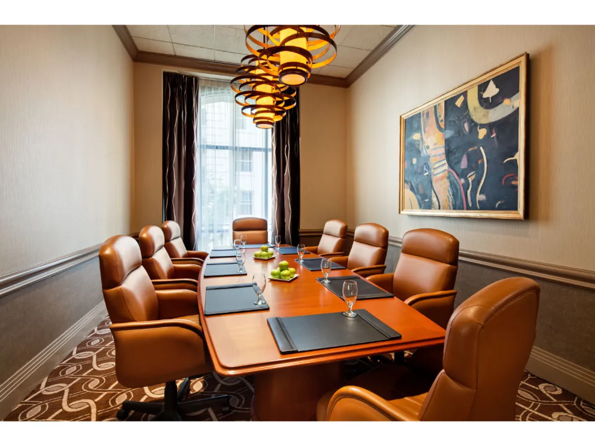 A conference room featuring a large table, elegant chandeliers, and tasteful artwork on the wall. The space exudes a professional yet inviting atmosphere, perfect for brainstorming sessions or negotiations.